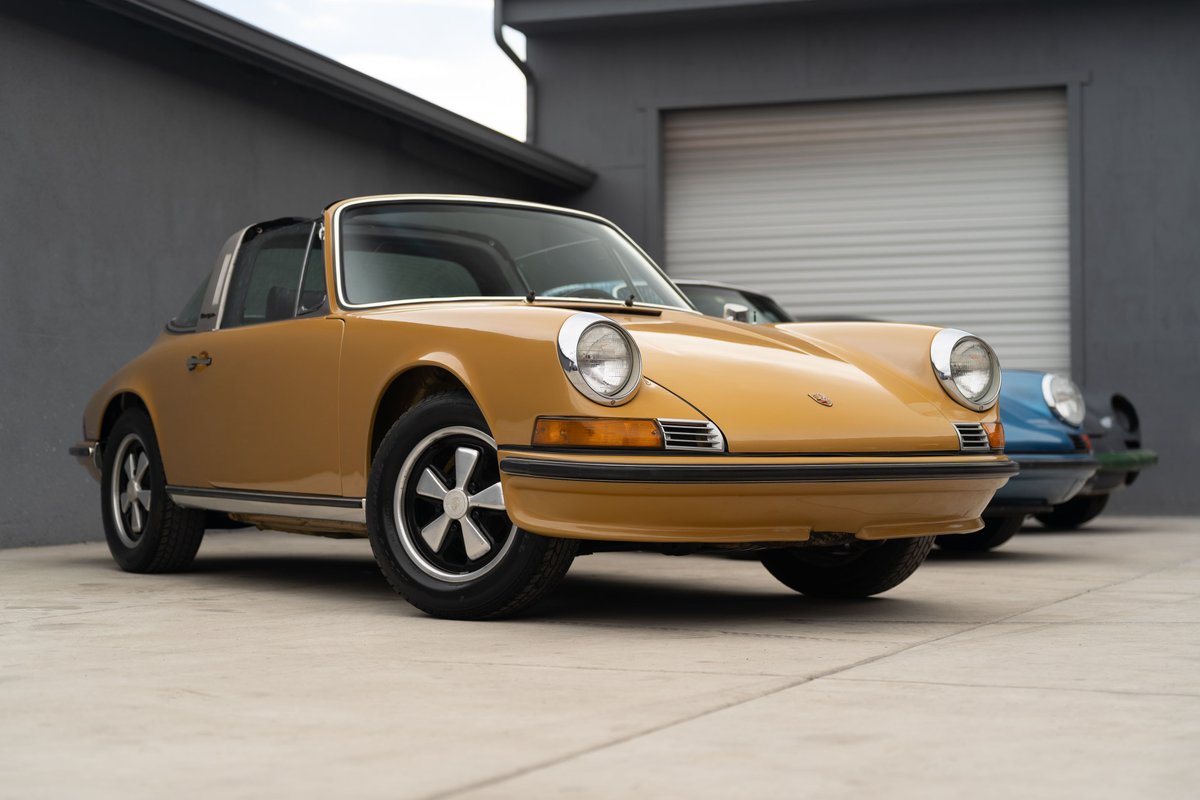 Yellow 1973 Porsche 911 Targa with Fuchs rims parked outdoors.