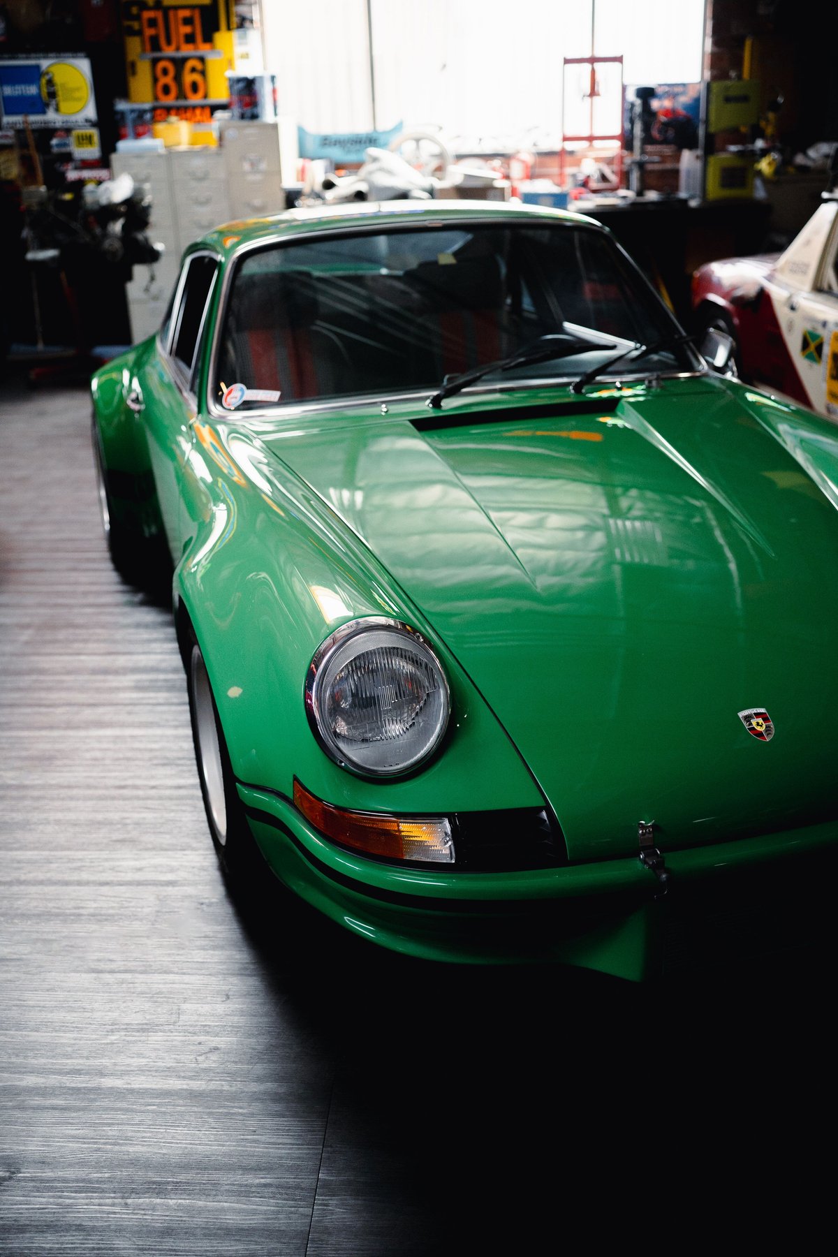 Green Porsche 911 Targa in a garage, showing its front fender, headlight, and chrome trim.