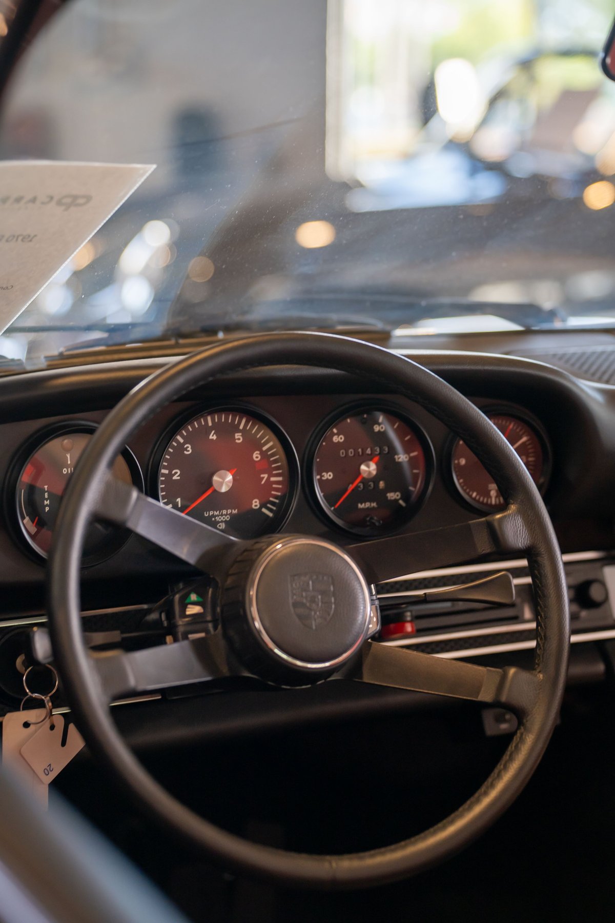 Close-up of a vintage Porsche 911 dashboard. Red-faced gauges, classic steering wheel with Porsche crest.