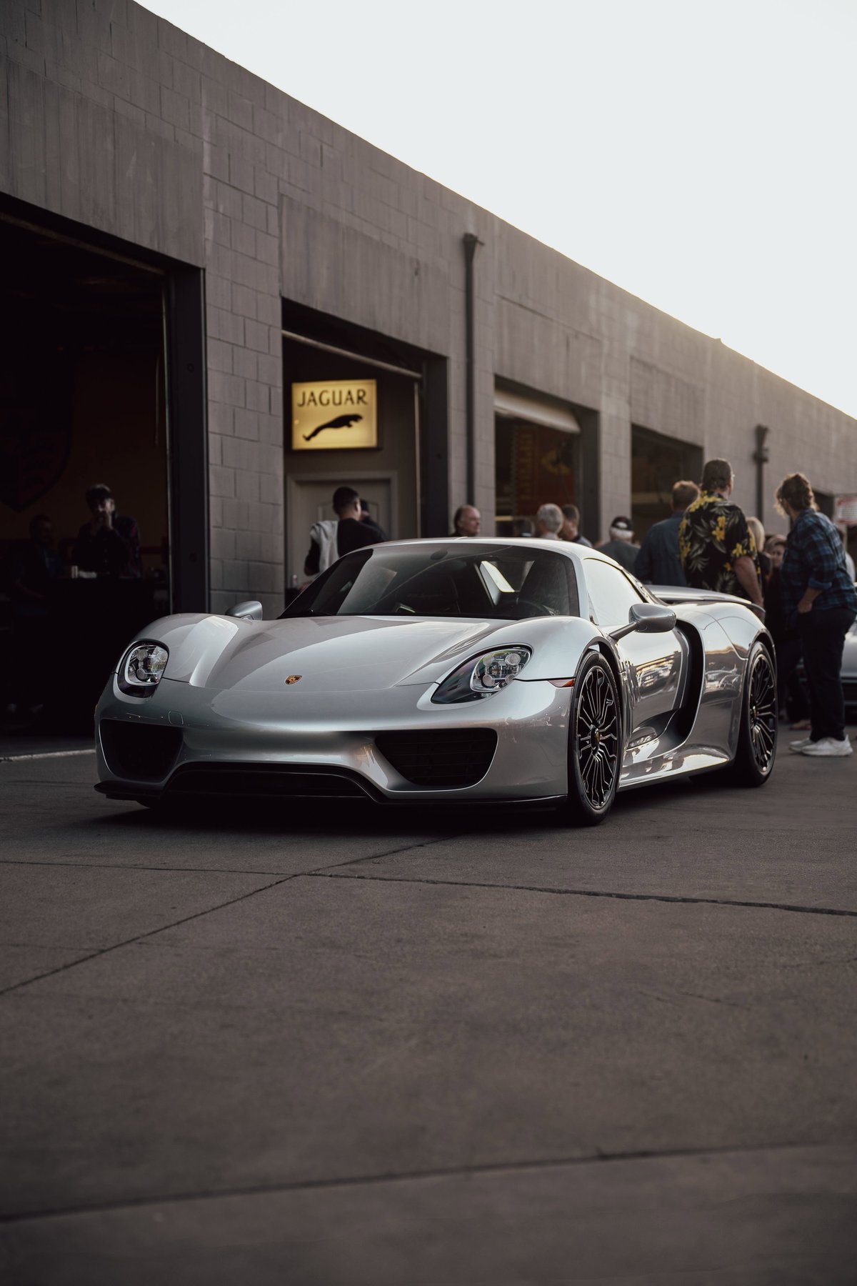 Silver Porsche 918 Spyder with black rims, parked outside Jaguar dealership.
