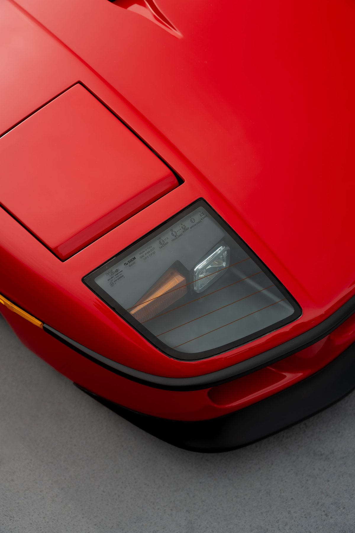 Close-up of a red Ferrari F40's pop-up headlight and glass engine cover.