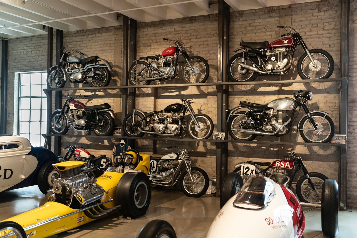 Vintage motorcycles and a yellow dragster on display shelves at the Lit Show Los Angeles 2024.