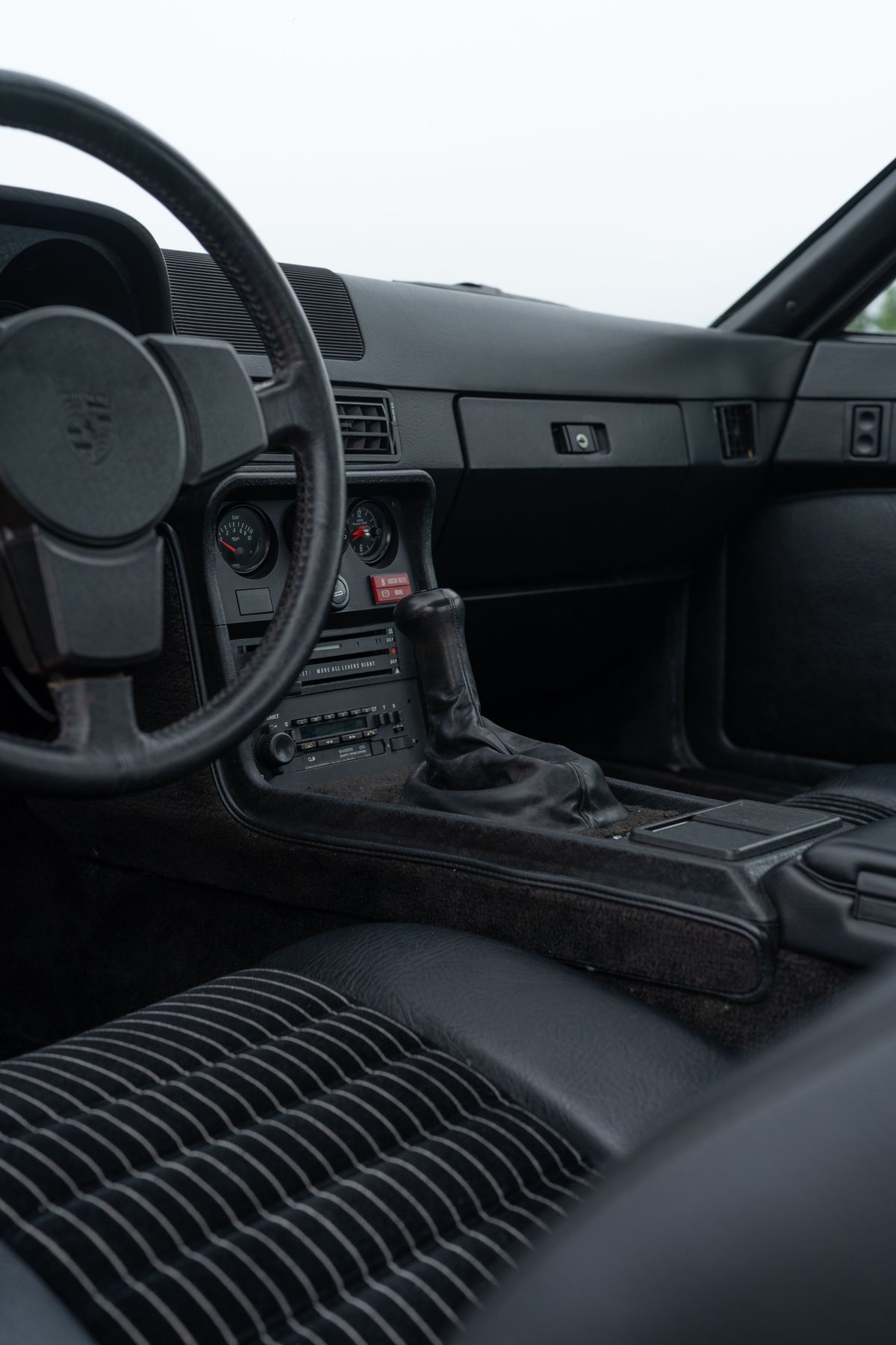 Interior shot of a 1981 Porsche 924 Turbo, black leather interior with striped seats and manual shifter.