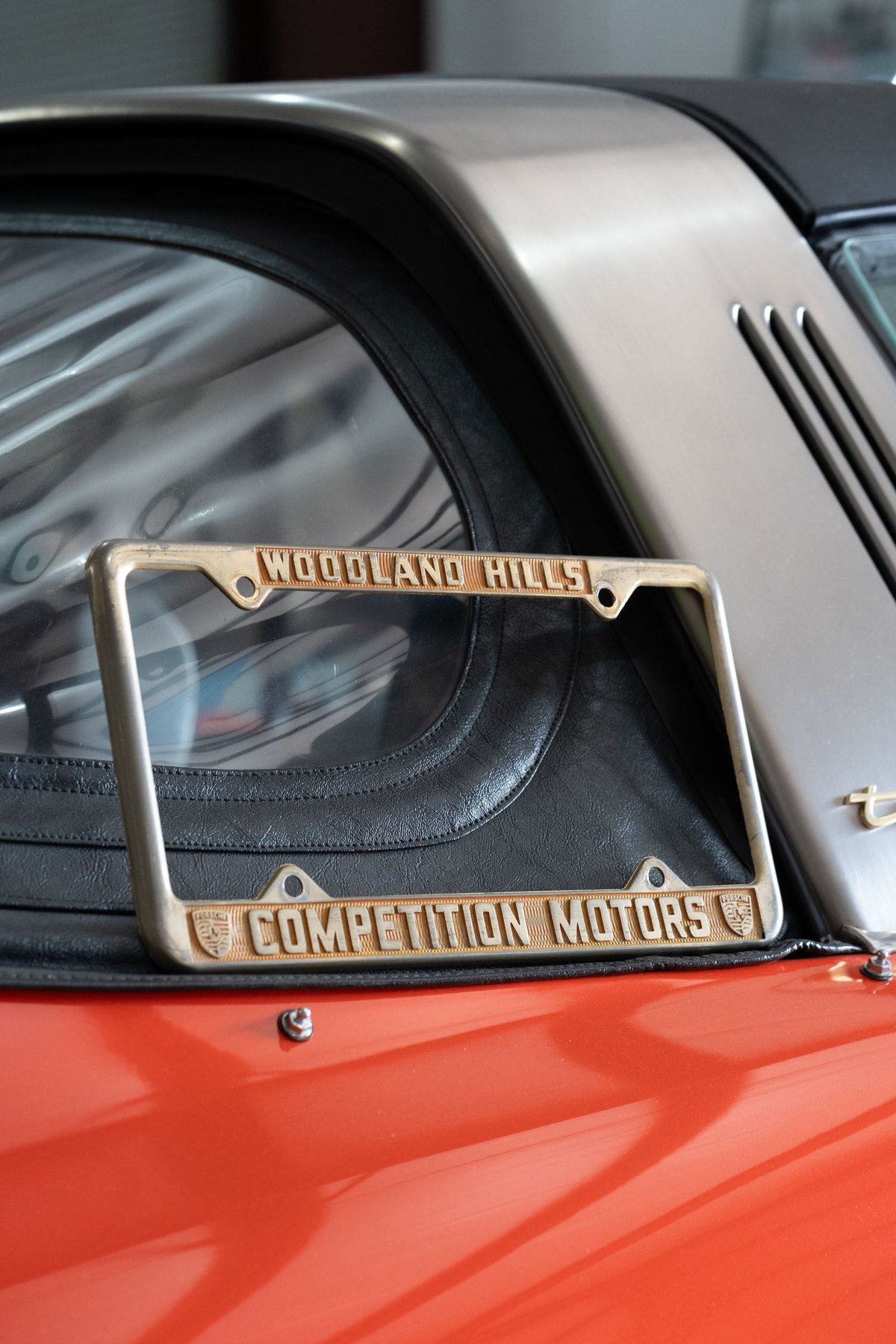 Vintage Porsche Targa with "Competition Motors" license plate frame, finished in orange.