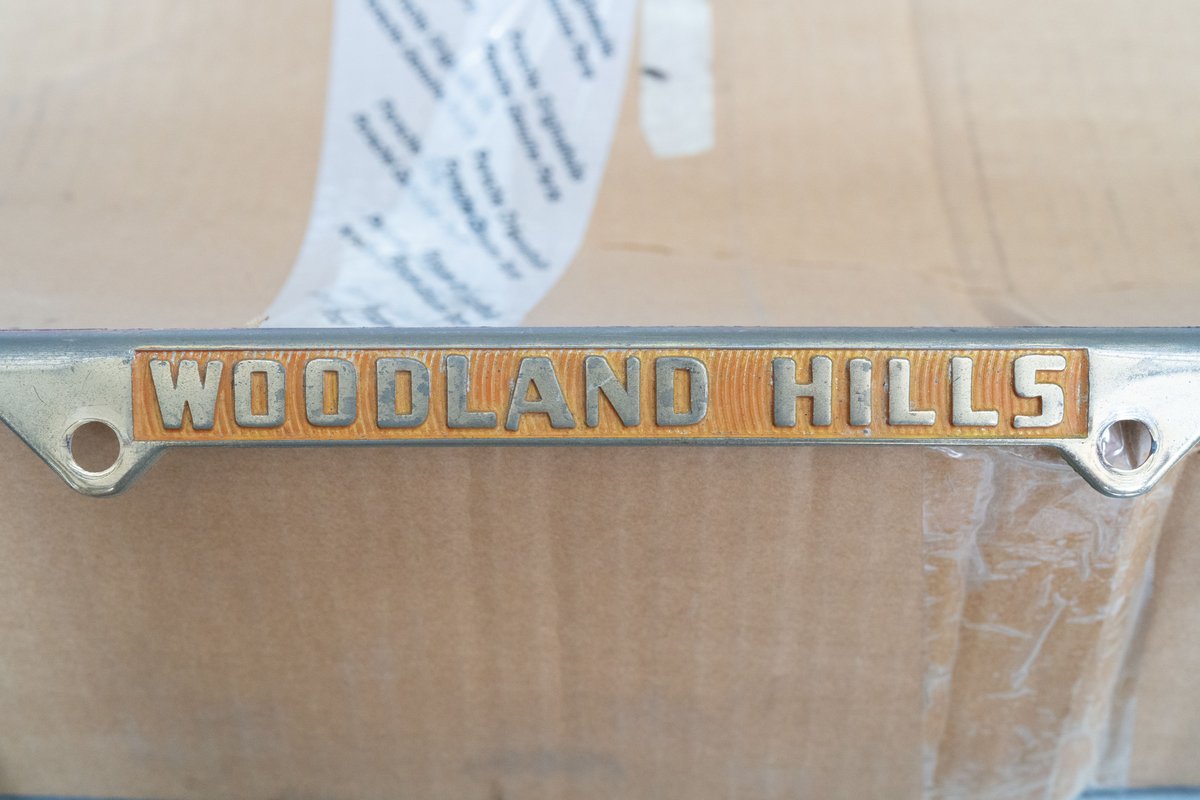 Chrome trim with "Woodland Hills" text in gold on a gold textured background, likely part of a car's livery.