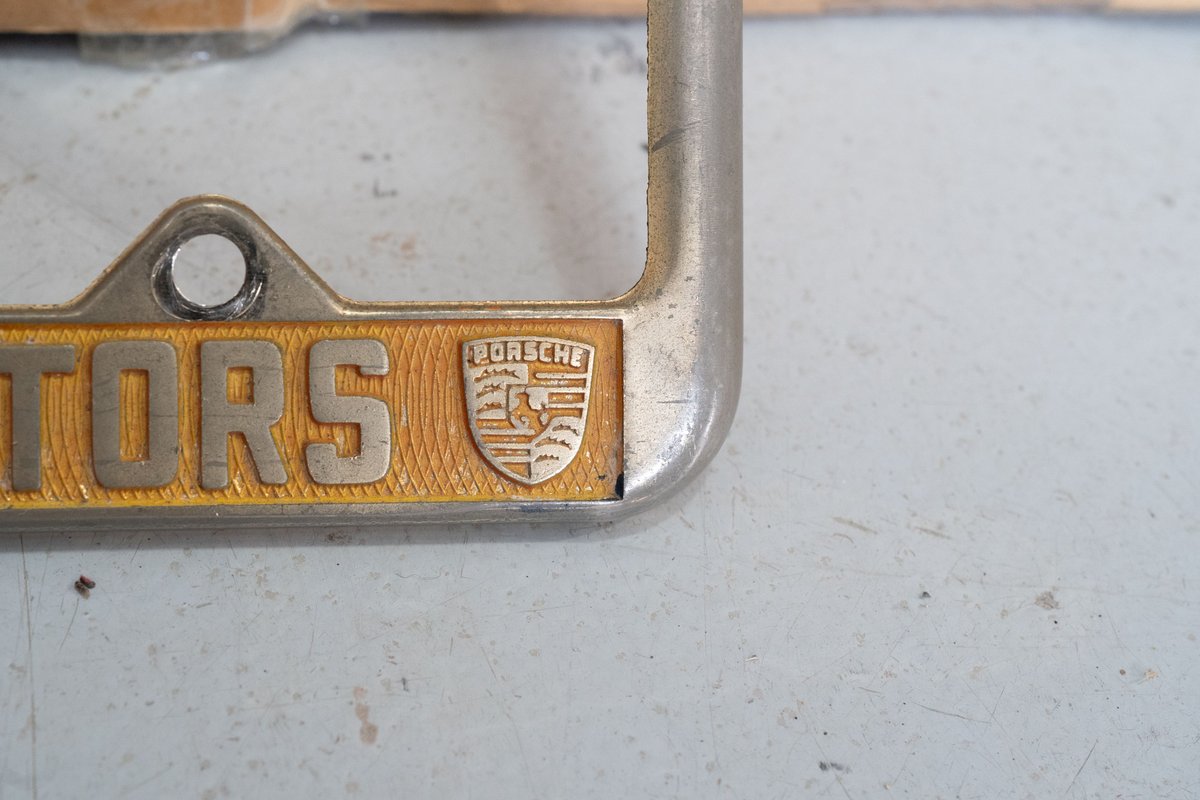 Silver Porsche license plate frame with gold trim and "TORS" text.