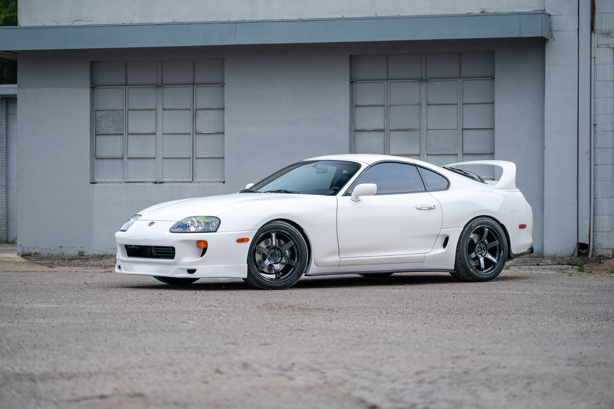 White 1994 Toyota Supra with aggressive body kit and aftermarket black rims.