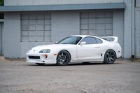 White 1994 Toyota Supra with aggressive body kit and aftermarket black rims.