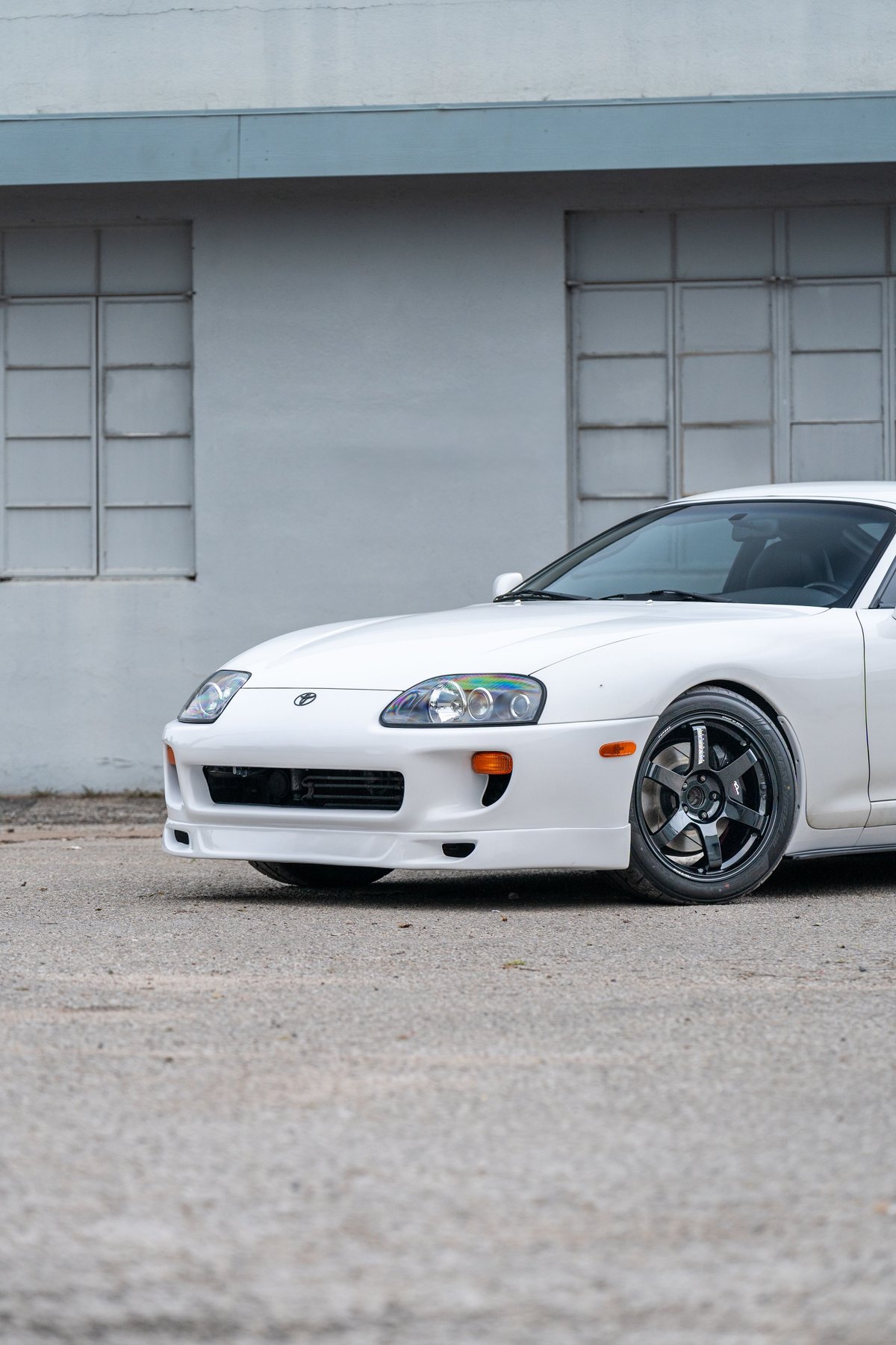 White 1994 Toyota Supra with aftermarket dark grey rims, parked on asphalt.