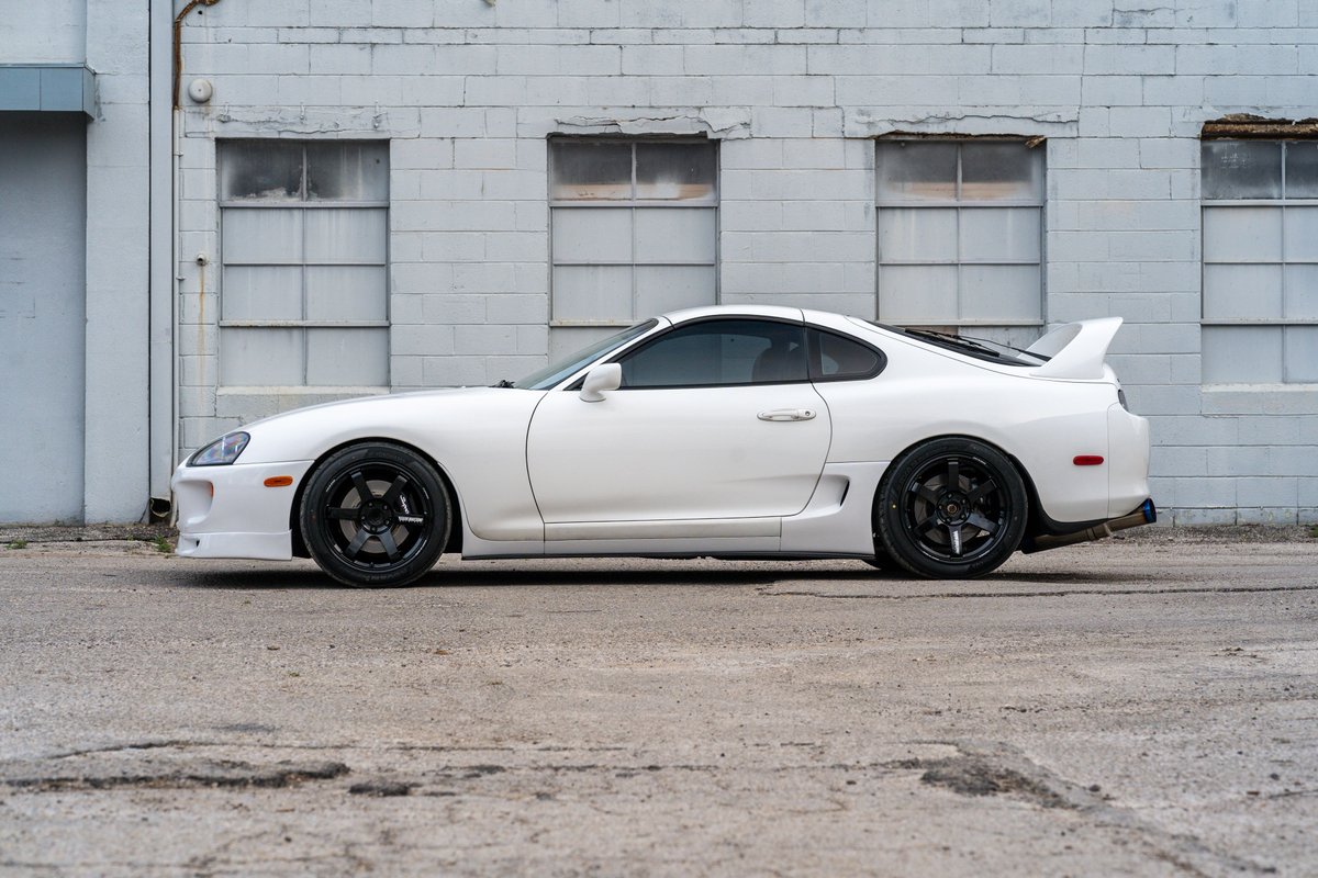 White 1994 Toyota Supra with black rims and a rear wing.