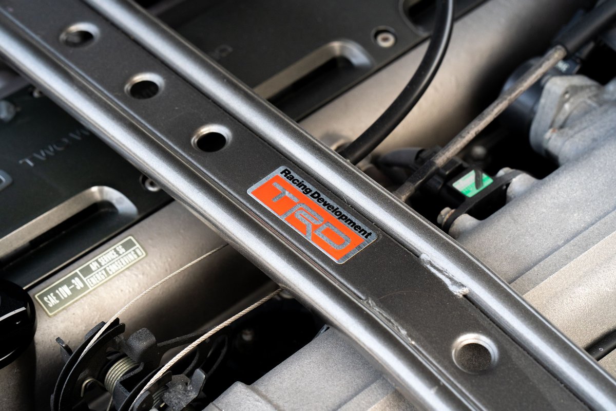 Close up of a TRD badge on a silver strut bar in the engine bay of a white 1994 Toyota Supra.