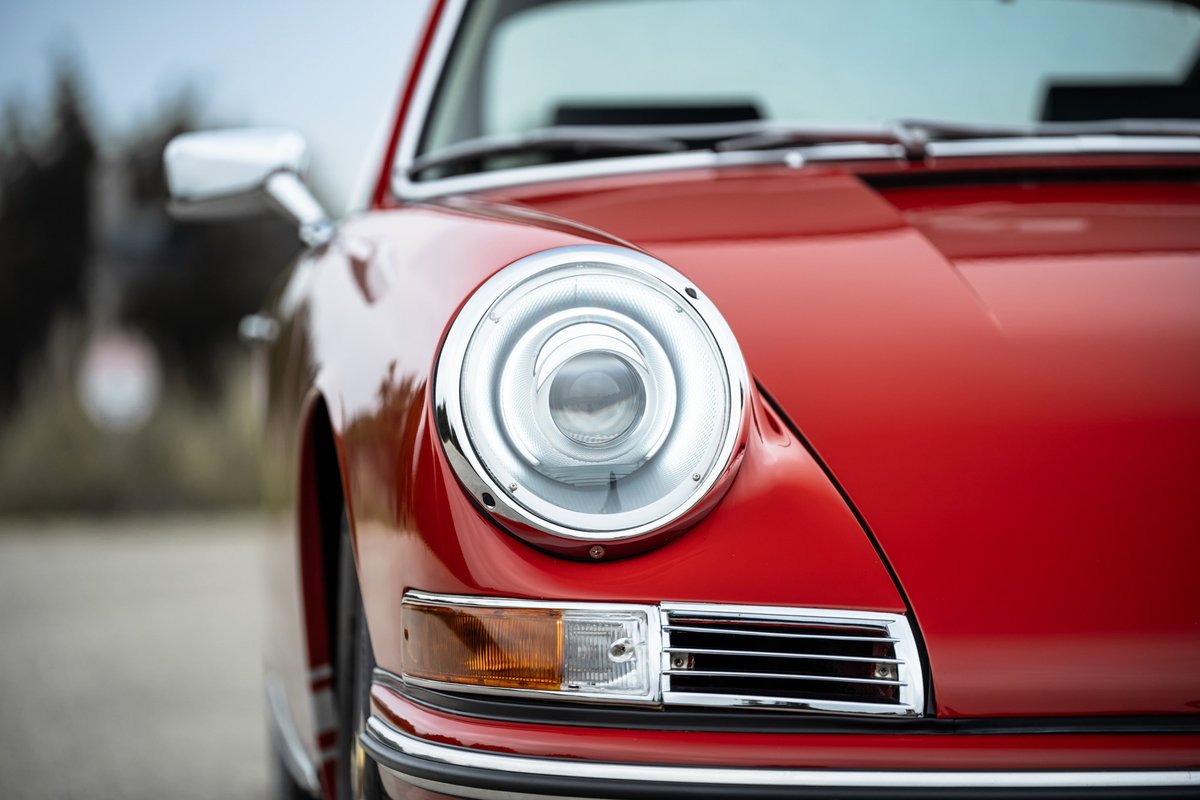 Close-up of a red 1967 Porsche 912 coupe's iconic headlight and chrome trim.