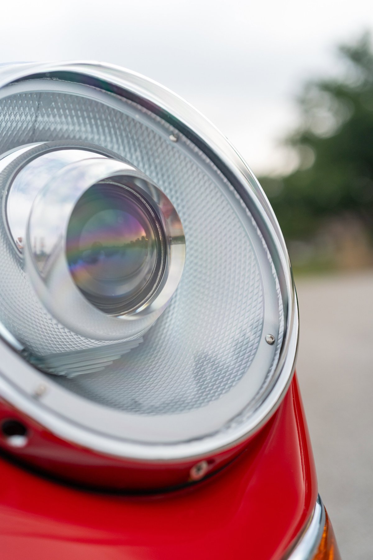 Close up of a vintage red Porsche 912 headlight with chrome trim.