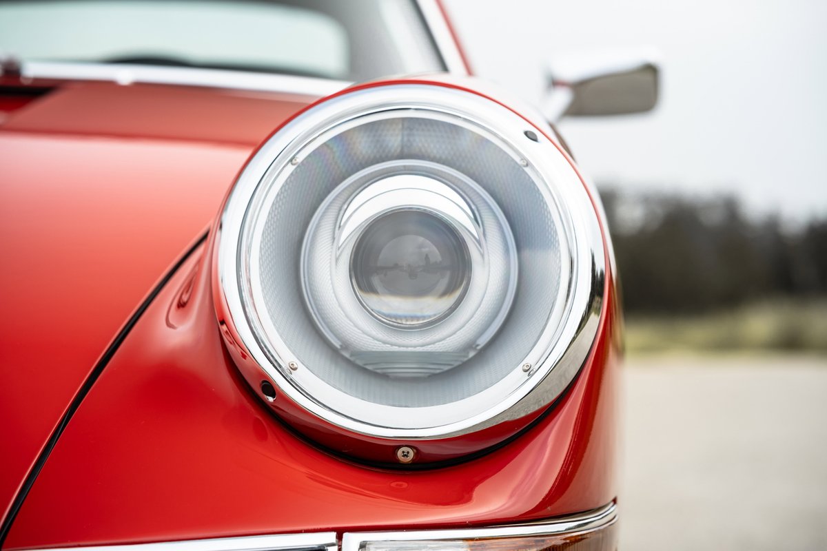 Close-up of a red 1967 Porsche 912 Coupe's chrome-trimmed headlight.