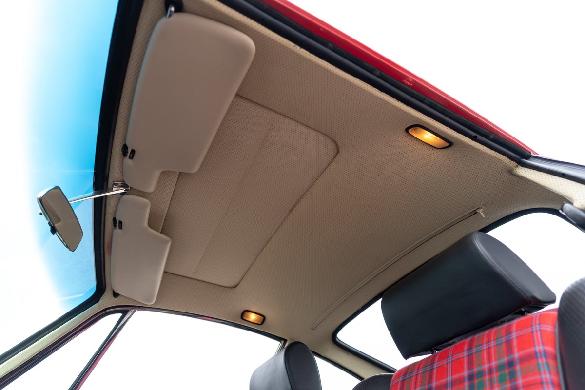 Interior view of a red 1967 Porsche 912 coupe with beige headliner, sun visors, and plaid seats.