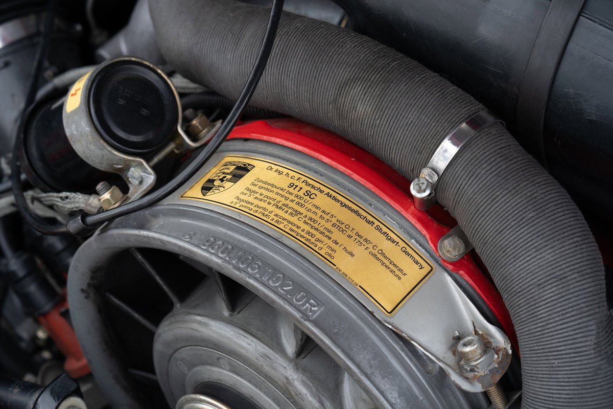 Porsche 911 SC engine bay, red trim, showing fan and air intake hose.