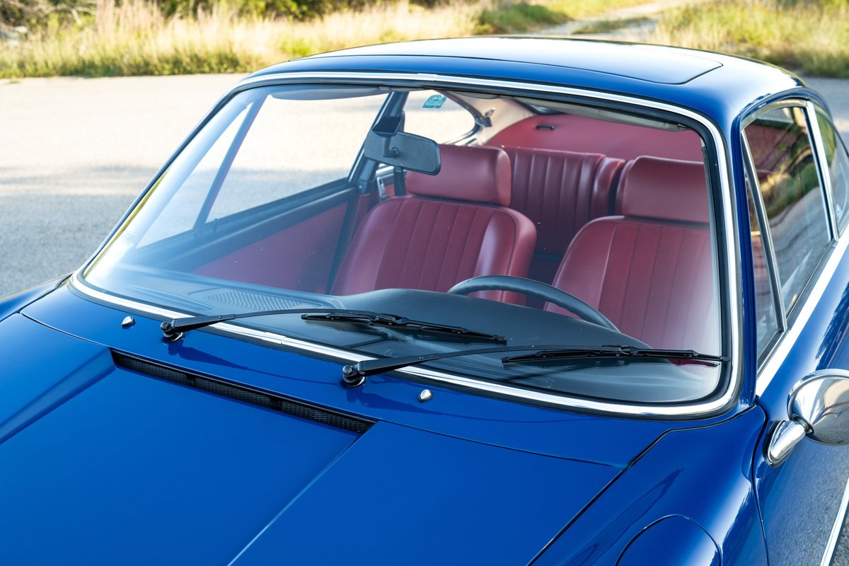 Close-up of a blue 1969 Porsche 911S with a red interior, showing the windshield, hood, and interior seats.