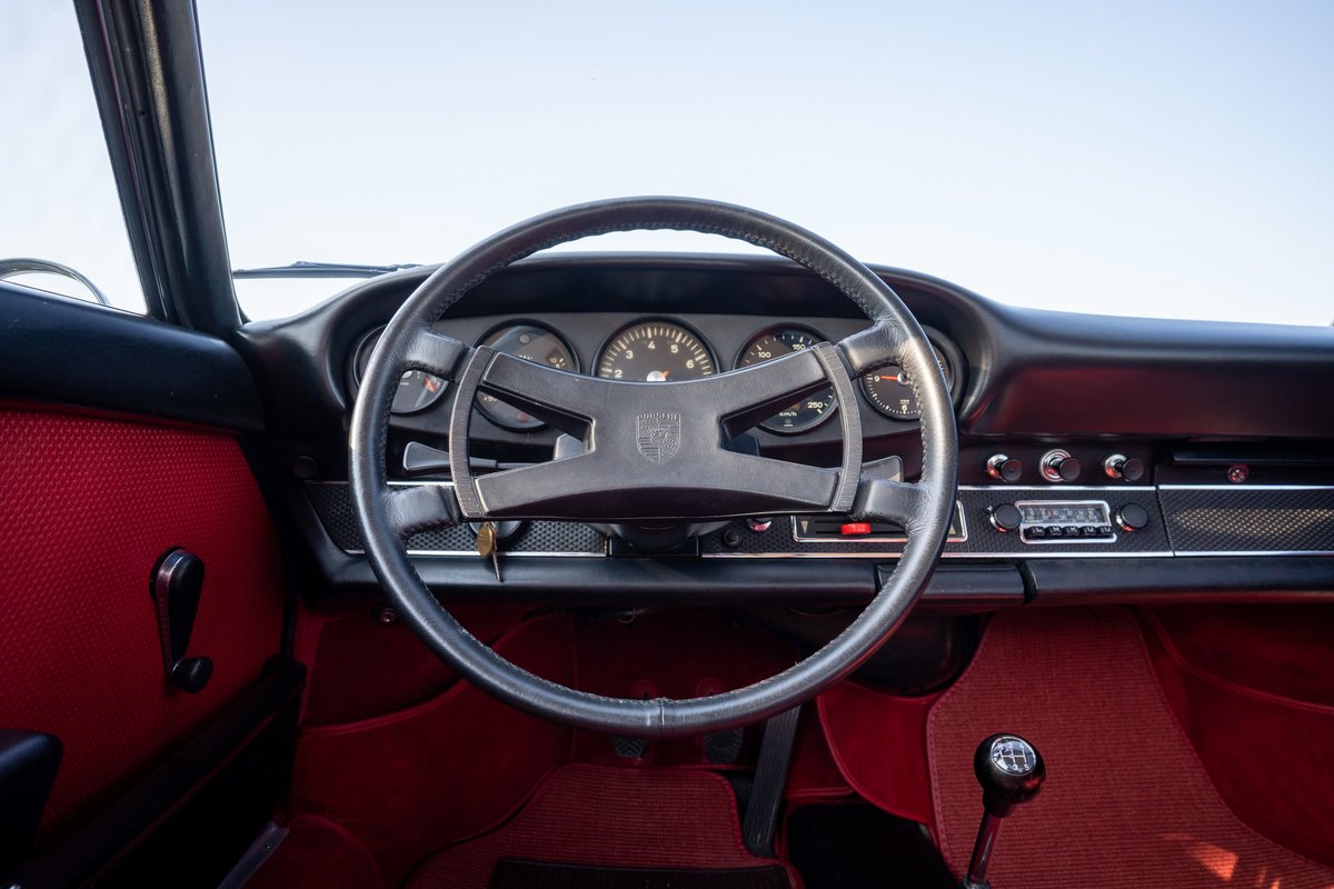 Interior of a blue 1969 Porsche 911S with red upholstery, black steering wheel, and original radio.