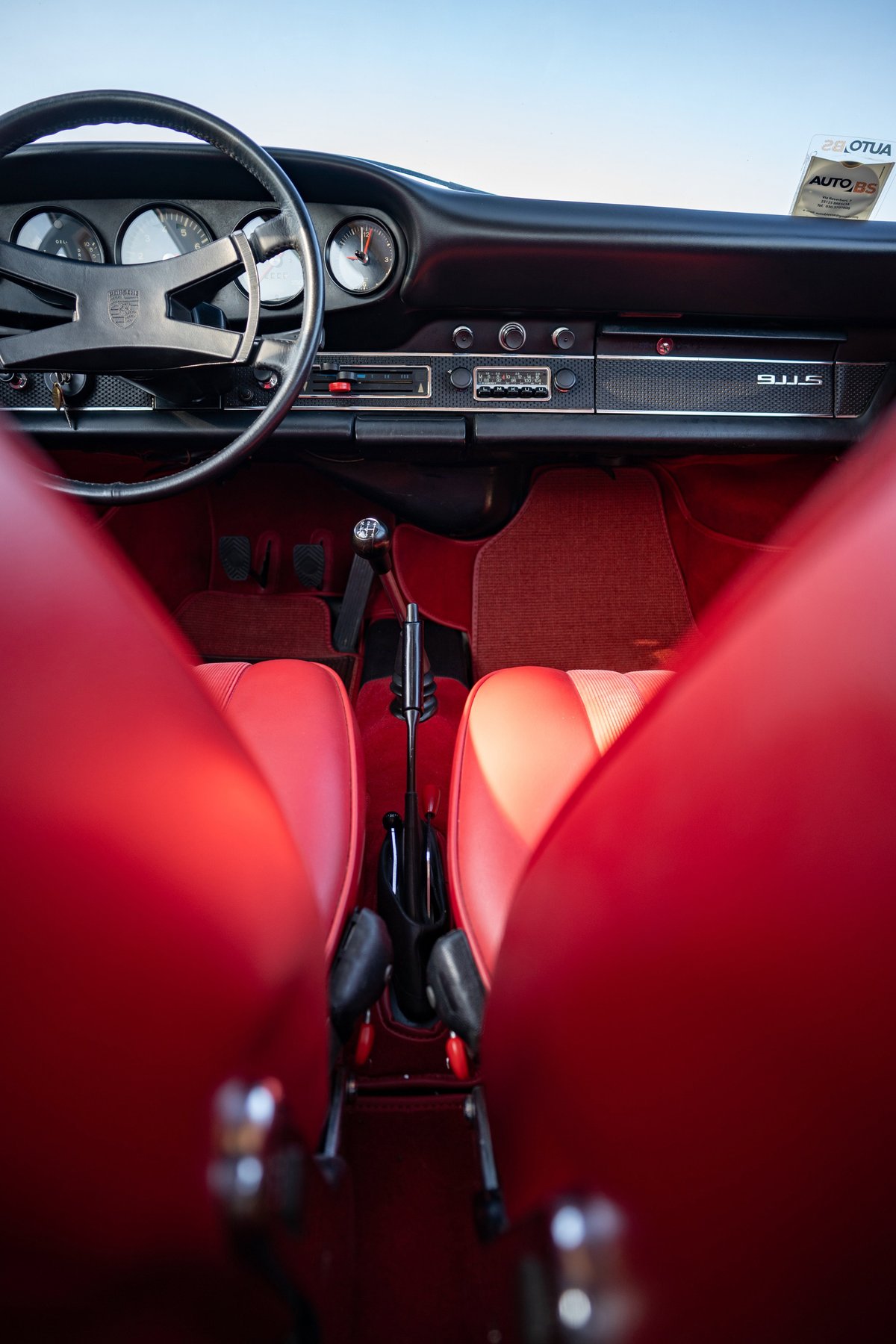 Interior view of a 1969 Porsche 911S with red leather seats, black steering wheel, and 5-speed shifter.