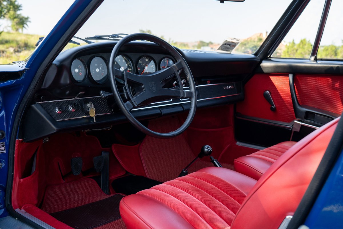 1969 Porsche 911S interior in blue with red seats and carpet. Dashboard gauges, steering wheel, gear shifter.