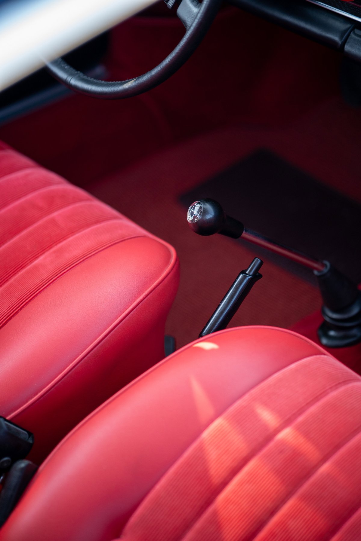 1969 Porsche 911S interior with red vinyl and corduroy seats, gear stick, and handbrake.