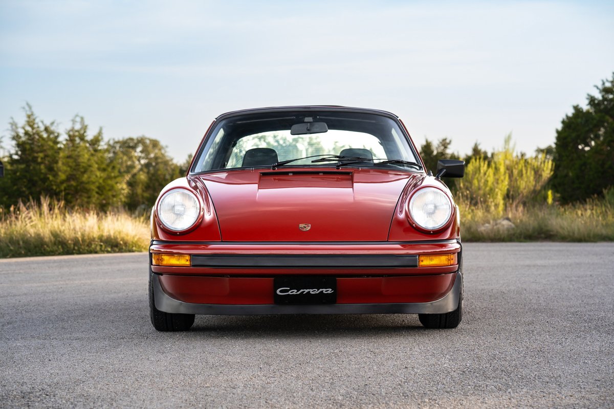 Front view of a red 1974 Porsche 911 Carrera Targa, showing its iconic circular headlights and black trim.