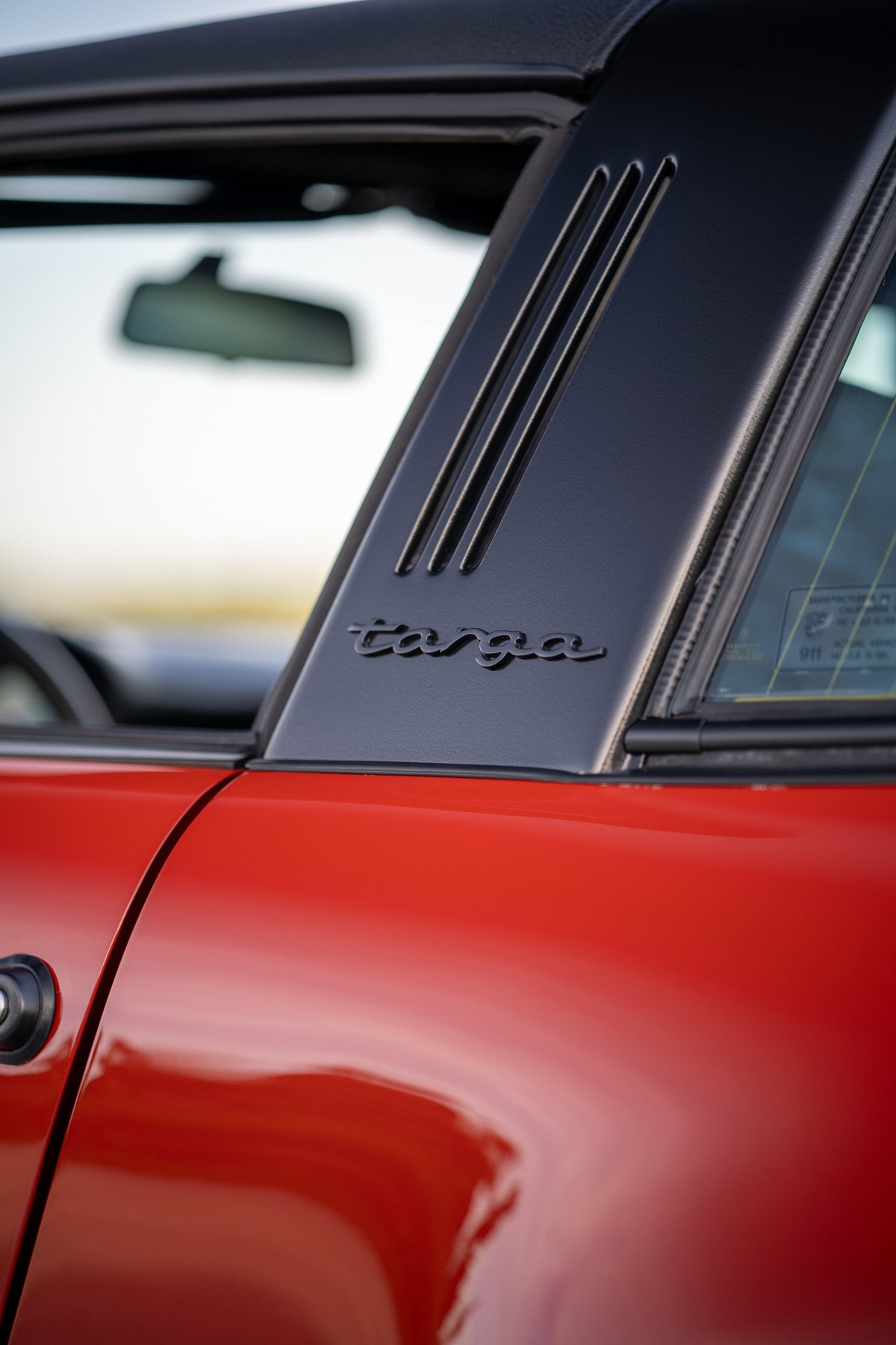 Close-up of a red 1974 Porsche 911 Carrera Targa B-pillar with black trim and badging.