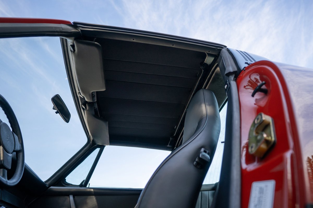 Red 1974 Porsche 911 Carrera Targa interior with open roof, black seats, and sun visors.