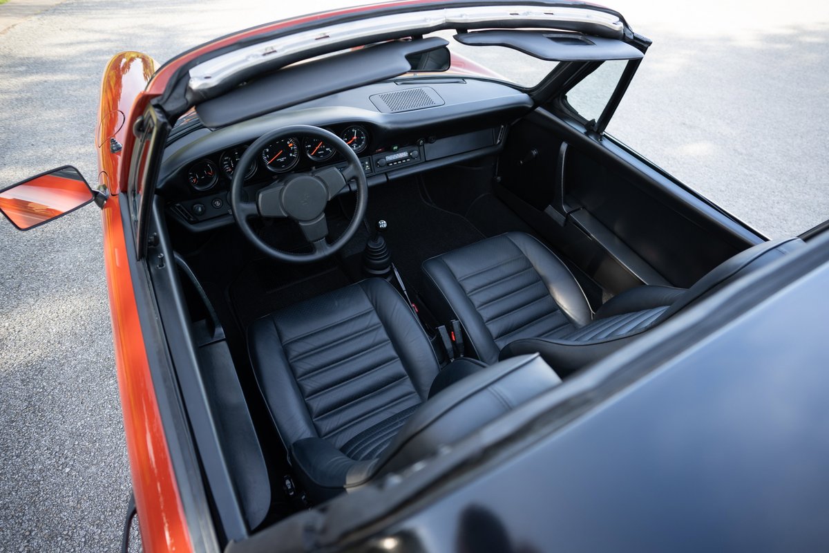 Interior view of a red 1974 Porsche 911 Carrera Targa with black leather seats and dashboard.