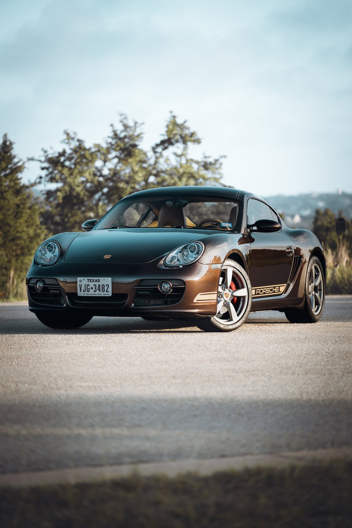 Brown 2008 Porsche Cayman S with gold livery and red brake calipers on alloy rims.