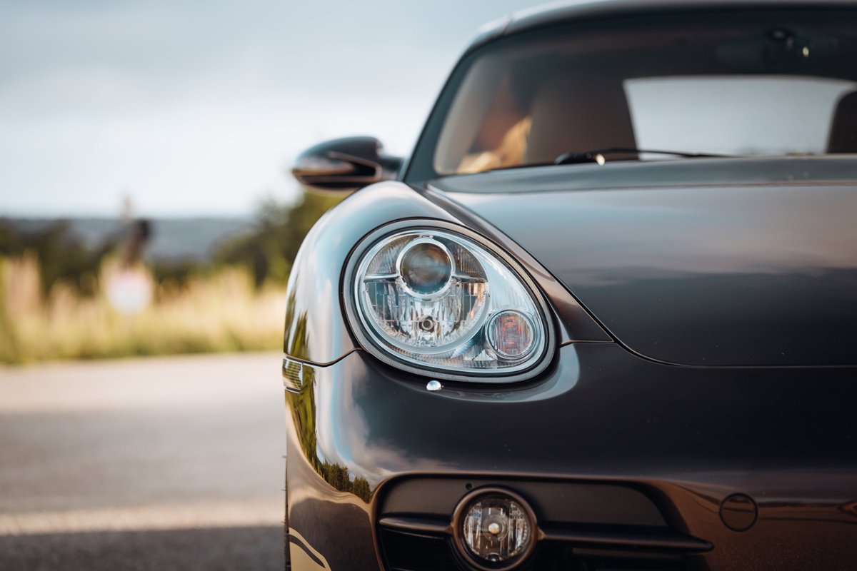 Close-up of a Macadamia Metallic 2008 Porsche Cayman S front-end, highlighting the projector headlight.
