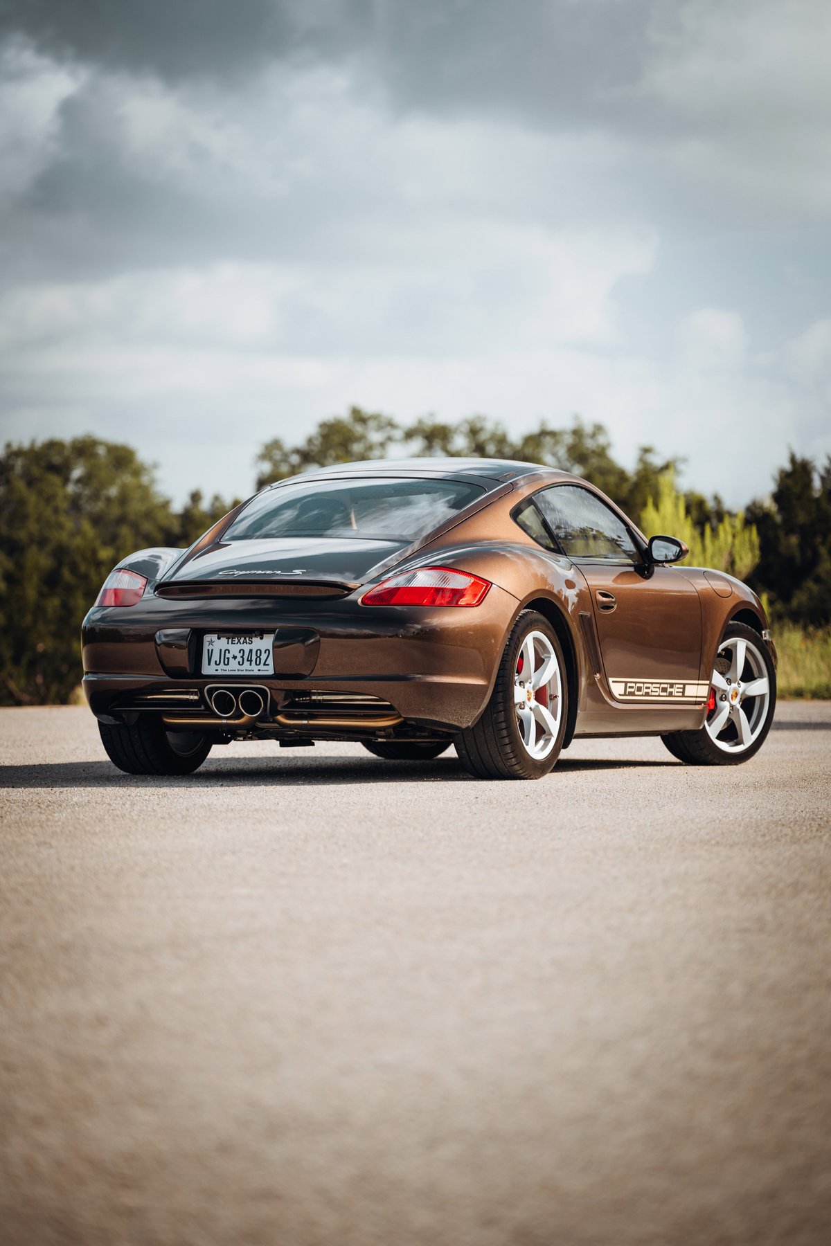 Brown 2008 Porsche Cayman S with chrome rims and a "Porsche" side livery.
