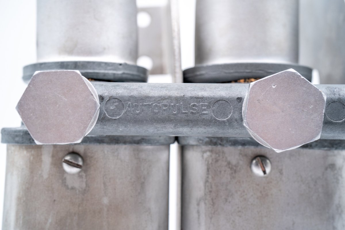Close-up of an "AUTOPULSE" branded aluminum fitting on a classic Porsche 550 Spyder part.