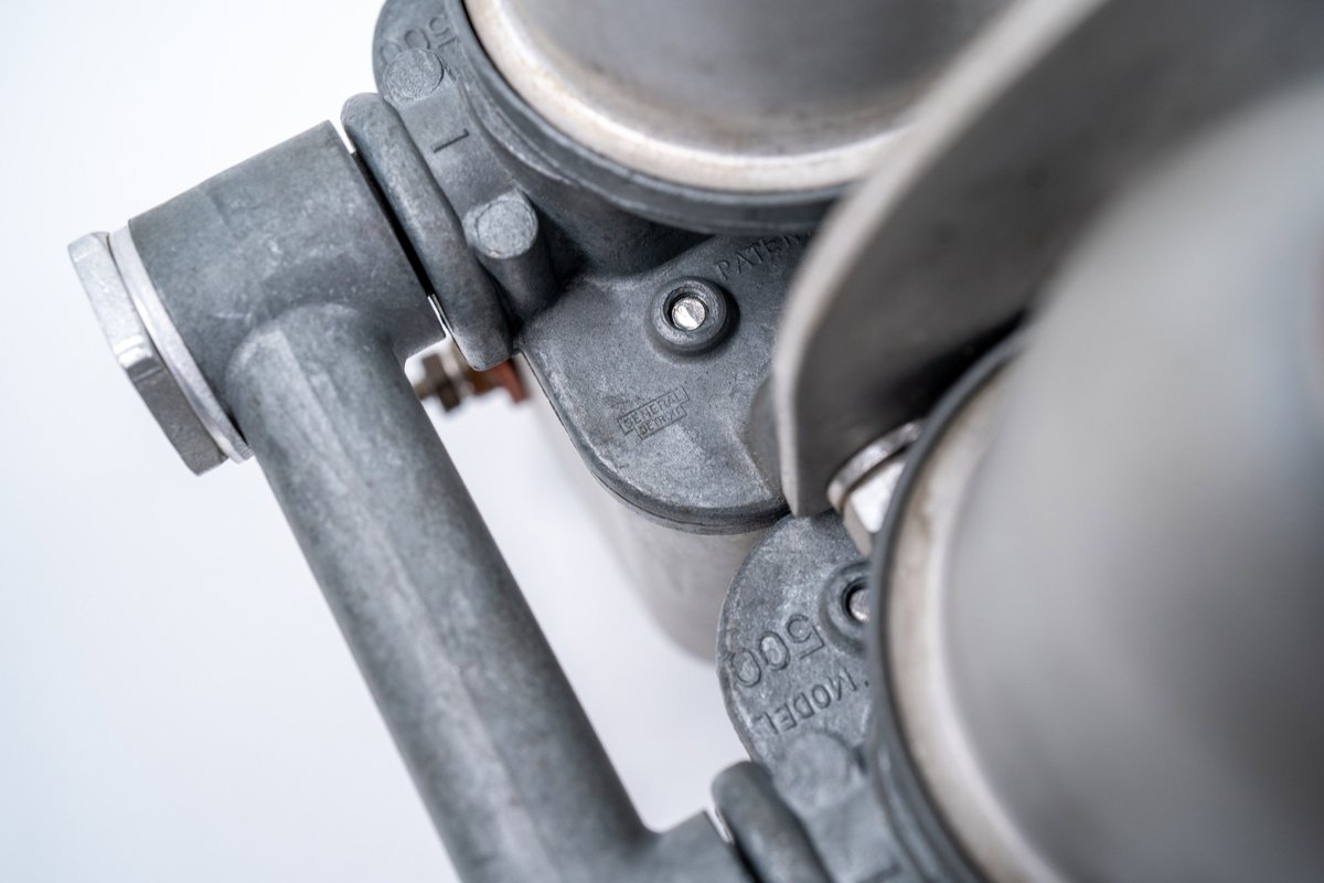 Close-up of a silver 1955 550 Spyder carburetor manifold with "MODEL 500" cast into the aluminum trim.