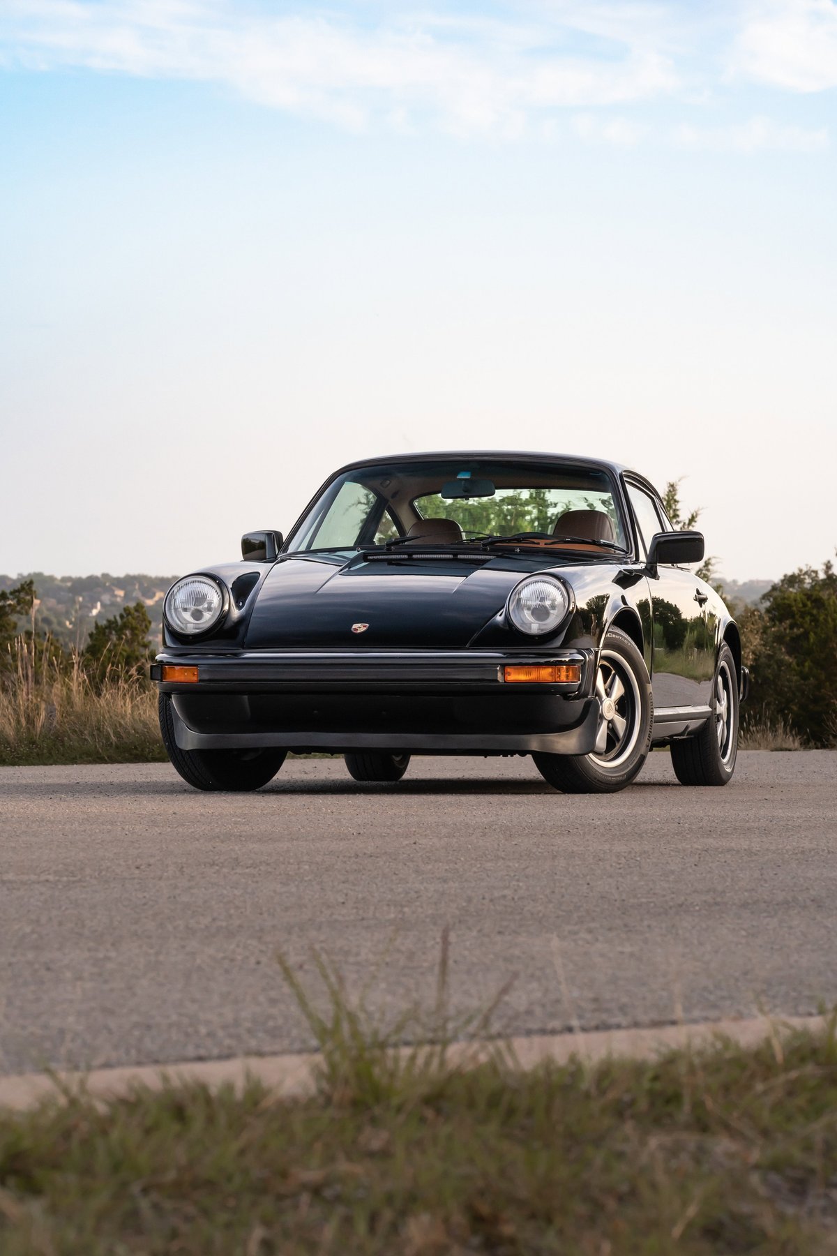 Front view of a black 1976 Porsche 911S with Fuchs rims and chrome trim.