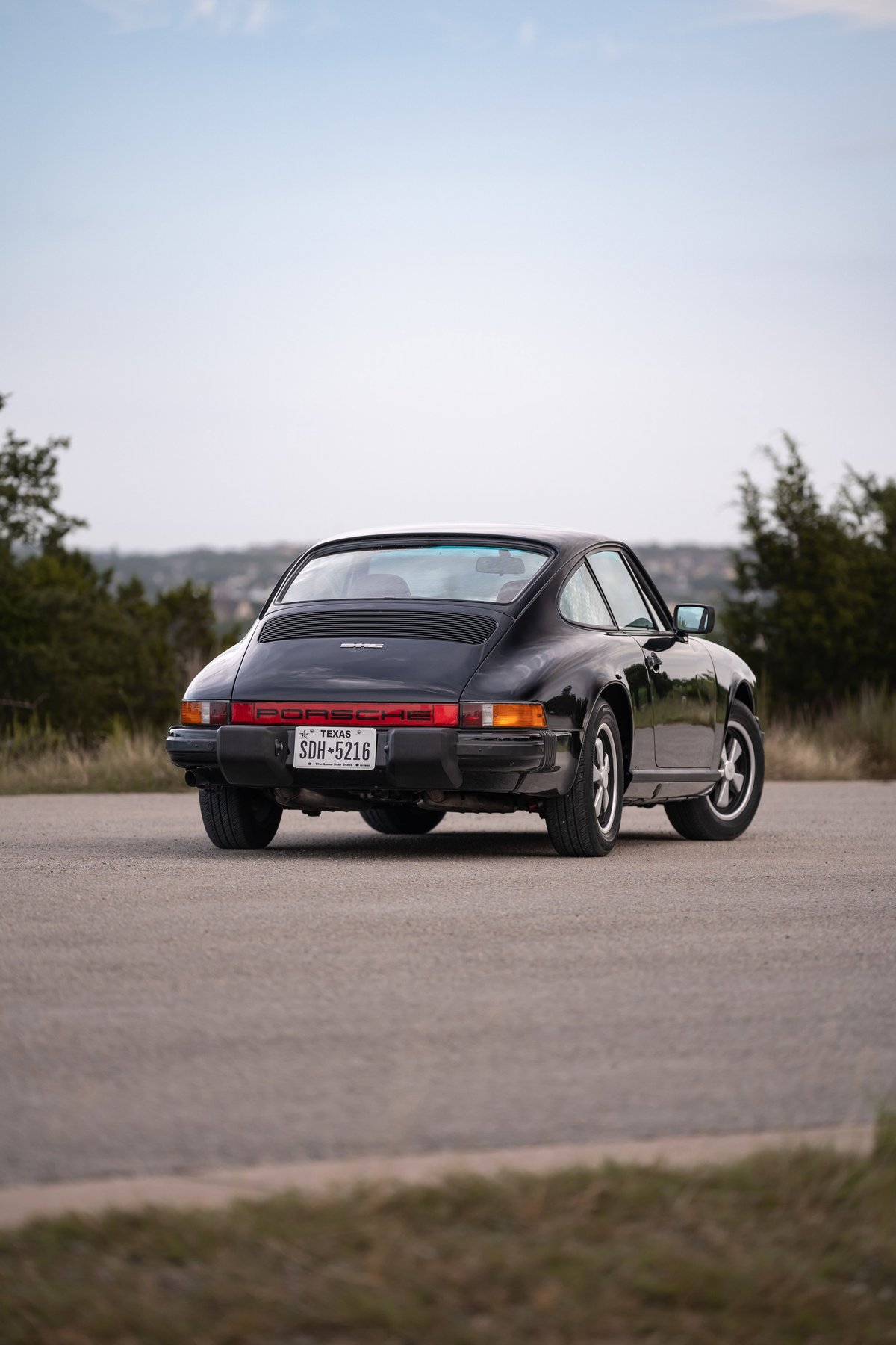 Rear view of a black 1976 Porsche 911S with Fuchs wheels on a paved road.