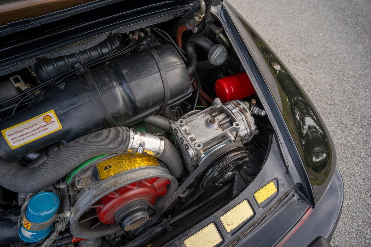 Close-up of a clean, black 1976 Porsche 911S engine bay, showing air-cooled flat-six, oil cooler, and intake.