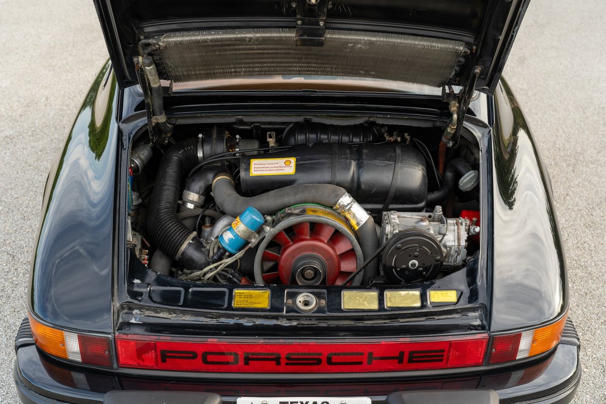 Black 1976 Porsche 911S Sportomatic engine bay with air-cooled flat-six engine and red fan.