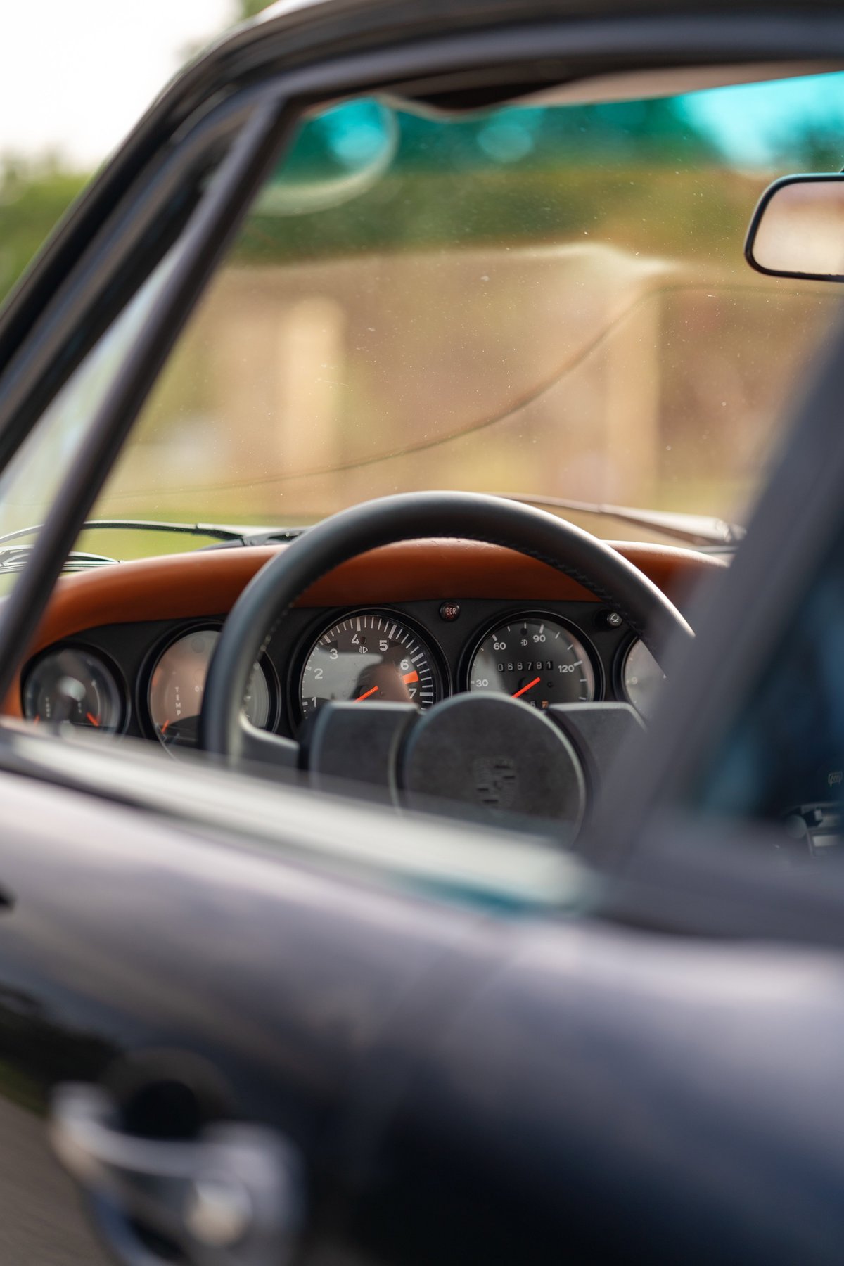 Close up of a black 1976 Porsche 911S Sportomatic interior, showing tan leather dash trim and analog gauges.