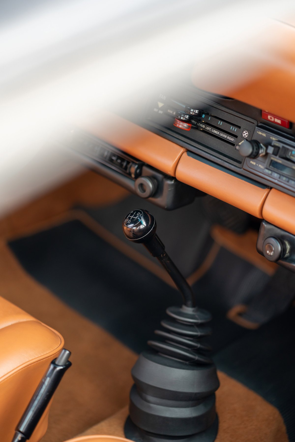 Close-up of a black 1976 Porsche 911S Sportomatic gear shifter, tan leather trim, and carpet.