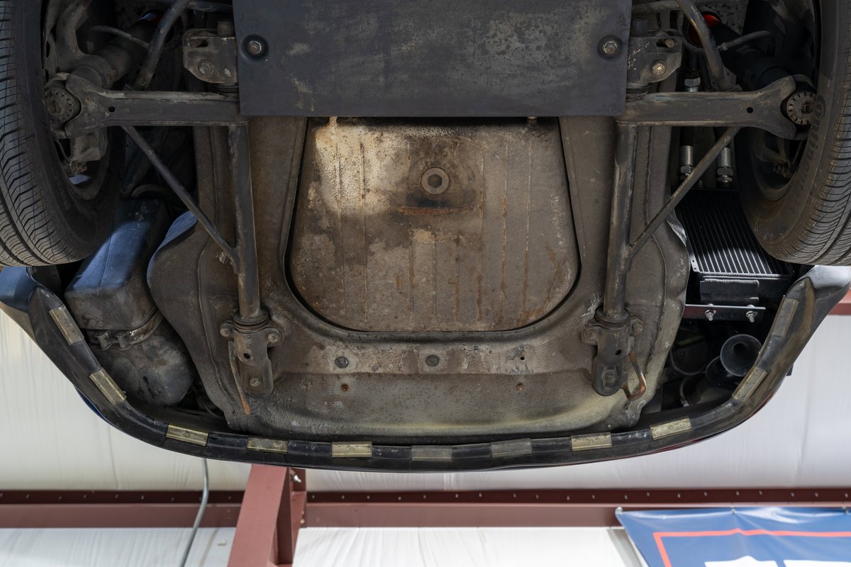 Underside of a black 1976 Porsche 911S Sportomatic showing fuel tank, exhaust, and suspension.