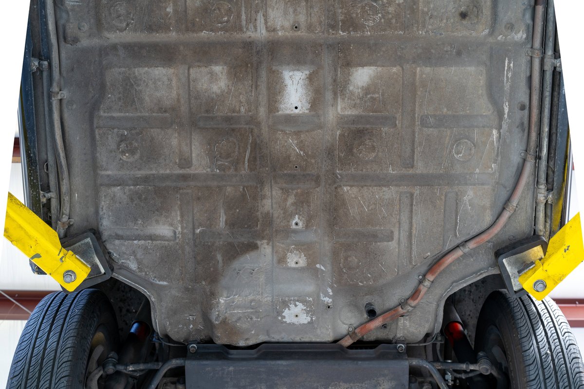 Underside of a black 1976 Porsche 911S Sportomatic on a lift, showing chassis and tire.