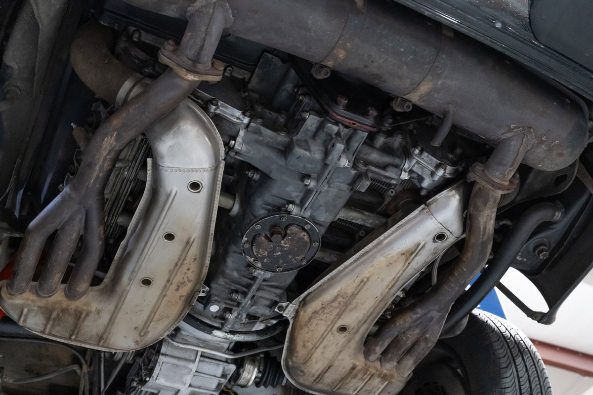 Underside view of a black 1976 Porsche 911S Sportomatic with dual exhaust pipes and engine.