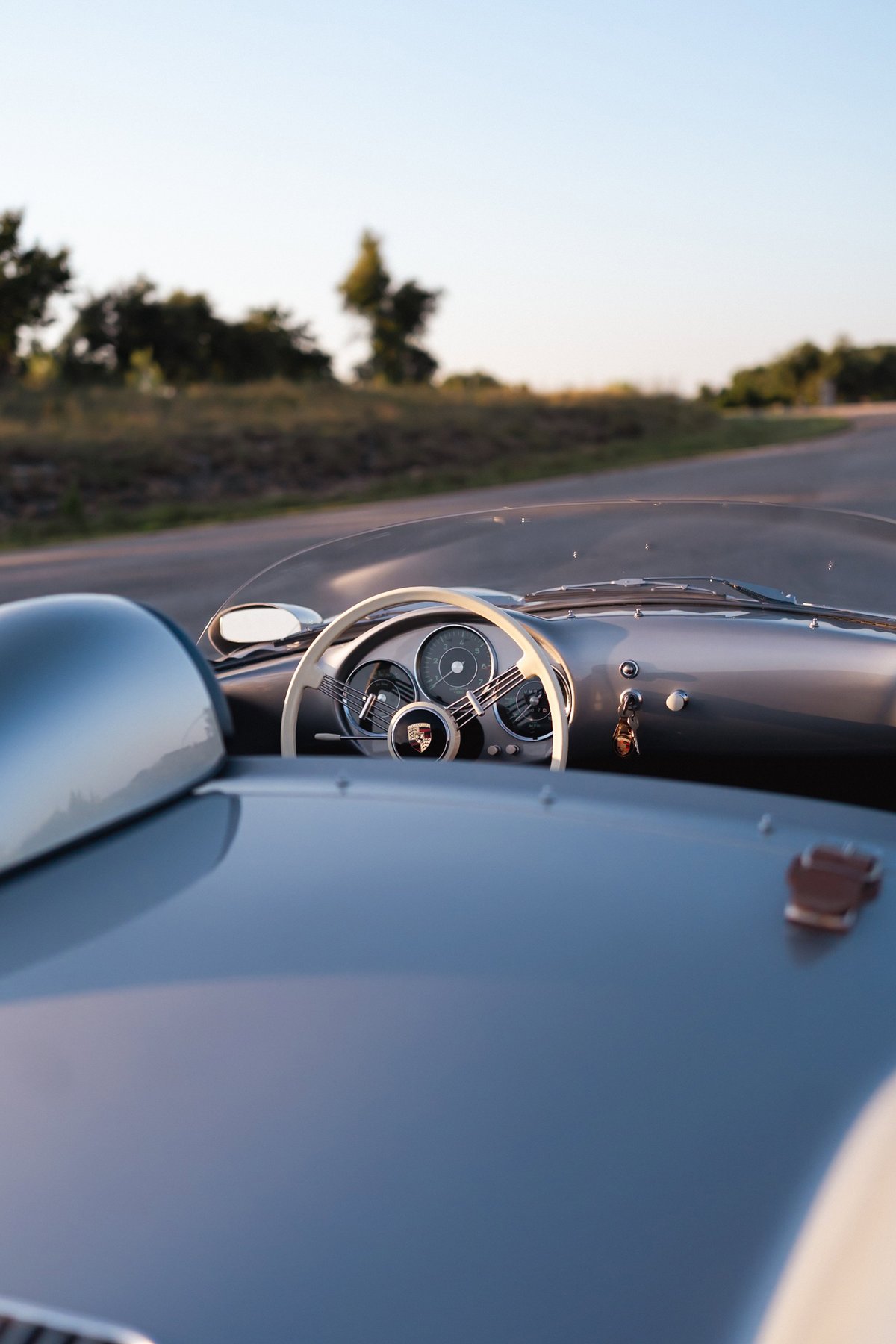 1955 Porsche 550 Spyder dashboard with white steering wheel, classic gauges, and grey body trim.