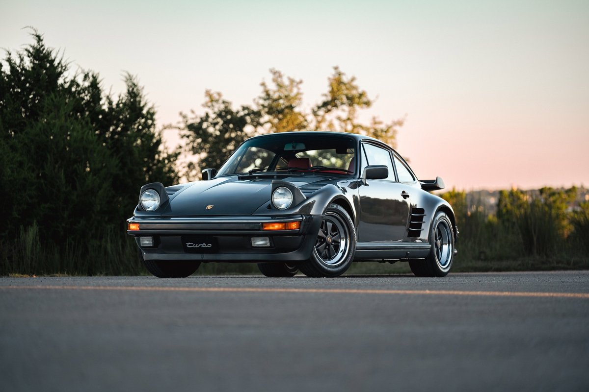 A slate grey metallic 1989 Porsche 930 Turbo Flachbau with black Fuchs rims and iconic whale tail spoiler.