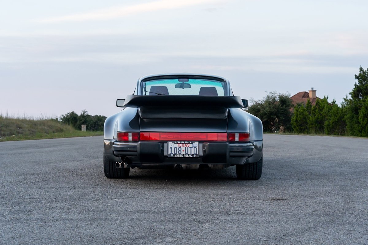 Rear view of a black Porsche 930 Turbo Flachbau with a whale tail spoiler and dual exhaust.