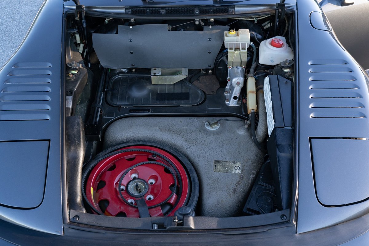 1989 Porsche 930 Turbo Flachbau front trunk with spare tire on red rim.