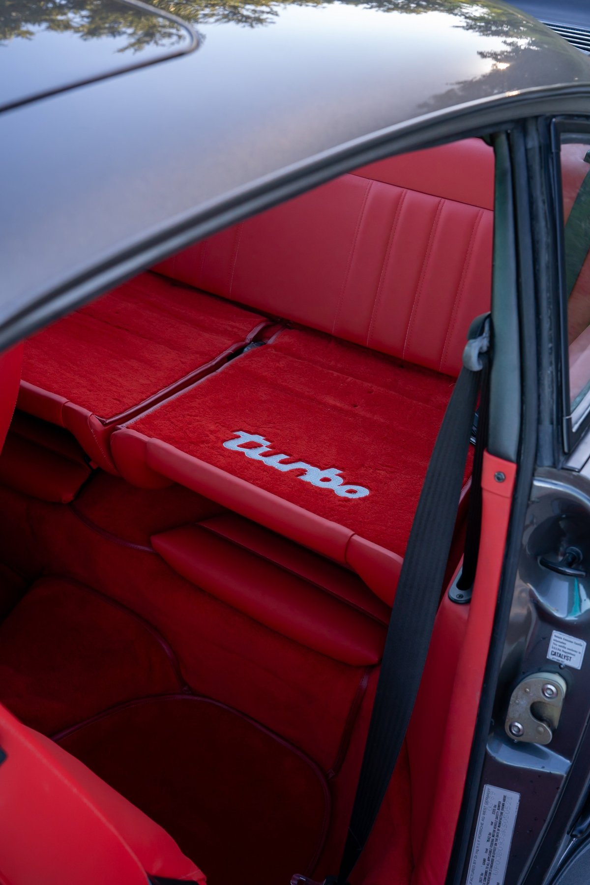 Close-up of a slate grey 1989 Porsche 930 Turbo Flachbau interior with red seats and "Turbo" embroidery.