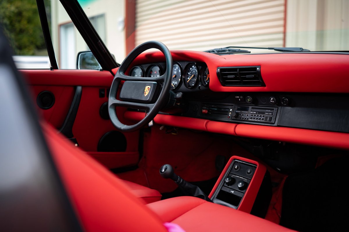 Interior view of a red 1989 Porsche 930 Turbo Flachbau with a black steering wheel and instrument cluster.