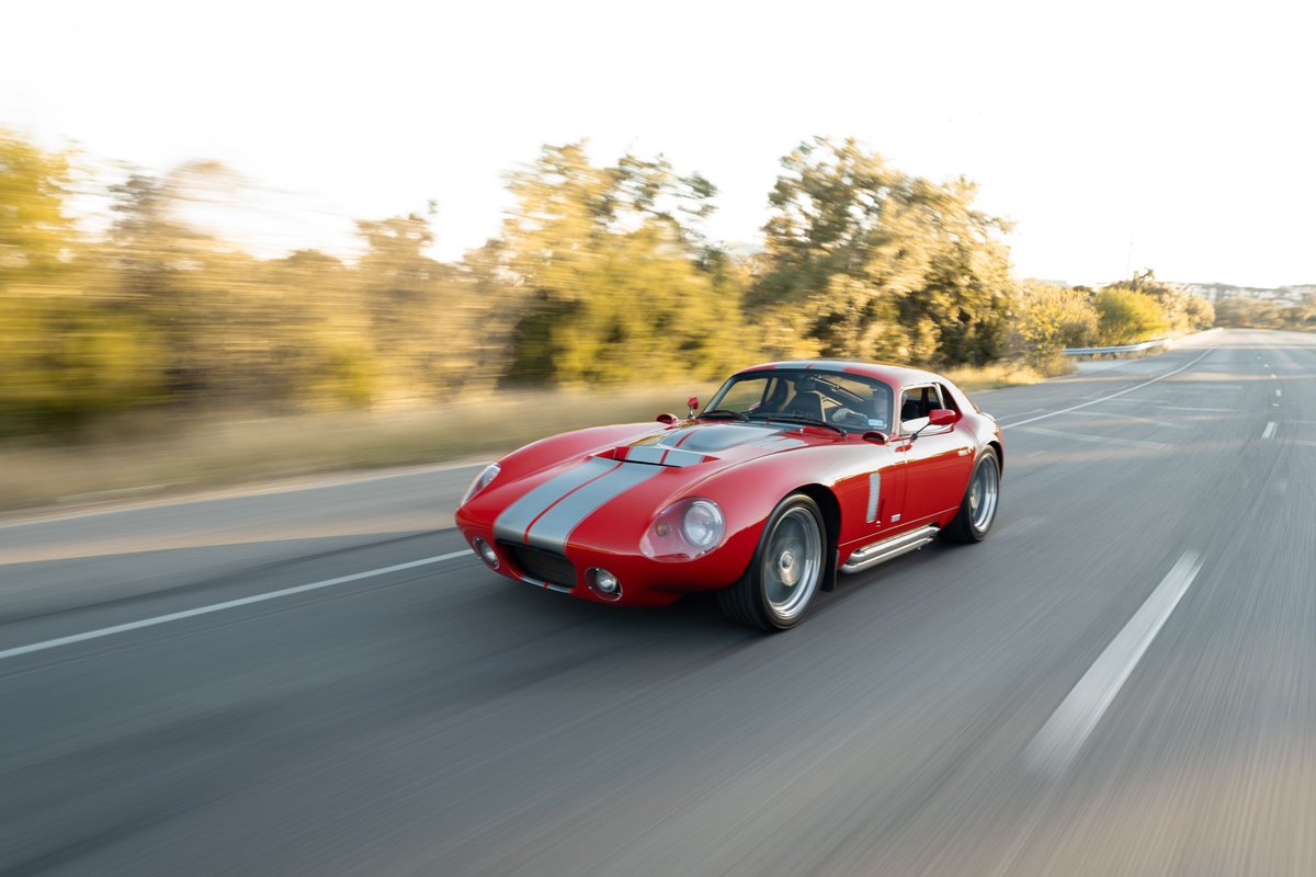 Red 1965 Superformance Shelby Daytona Coupe with silver racing stripes and polished rims.